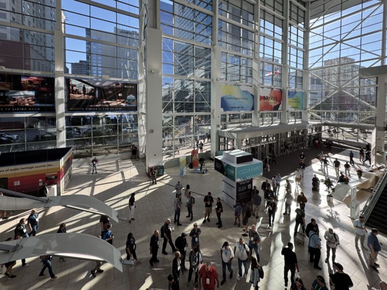 Convention center floor with high vaulted ceilings and windowed walls on all sides. People mill about.