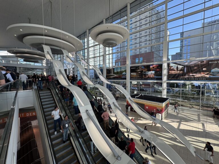 Large convention center escalaor bank with windows showing more hotels outdoors, people on the escalators, and ads for Sony.