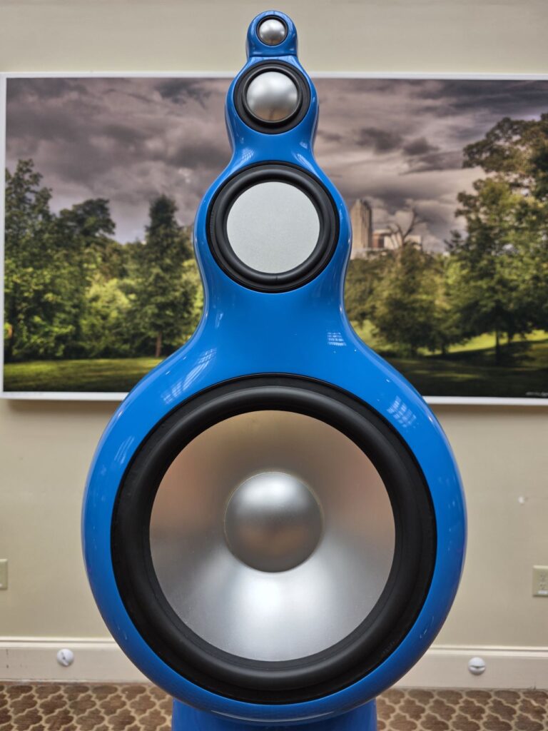 Closeup on the top of a speaker showing a tower of three circles surrounded by a blue wave, with a painting in the background.