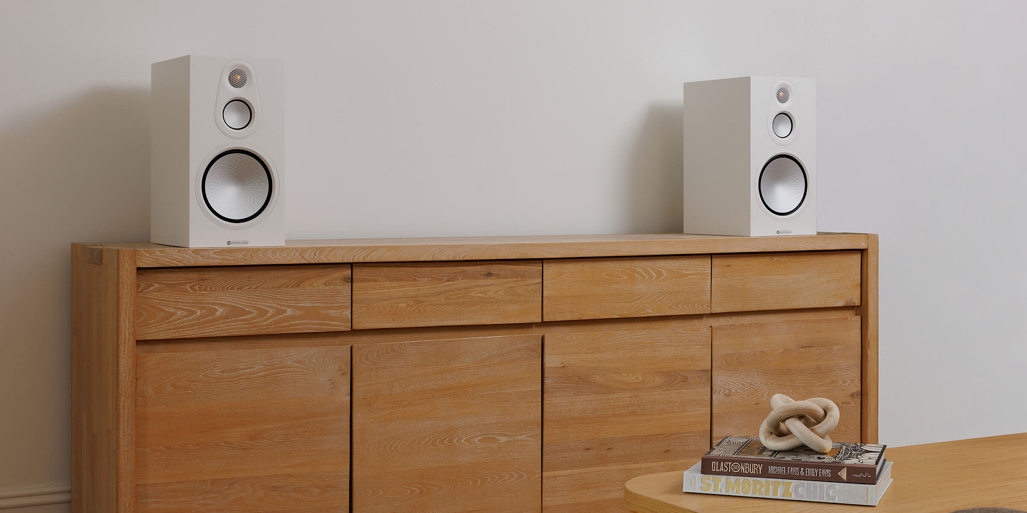 Pair of white Monitor Audio Silver 100 8G three-way stand-mount speakers on a wood cabinet.