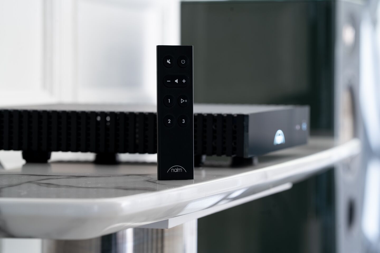 Naim CI-Uniti 102 on raised feet with its Bluetooth remote standing on a shelf