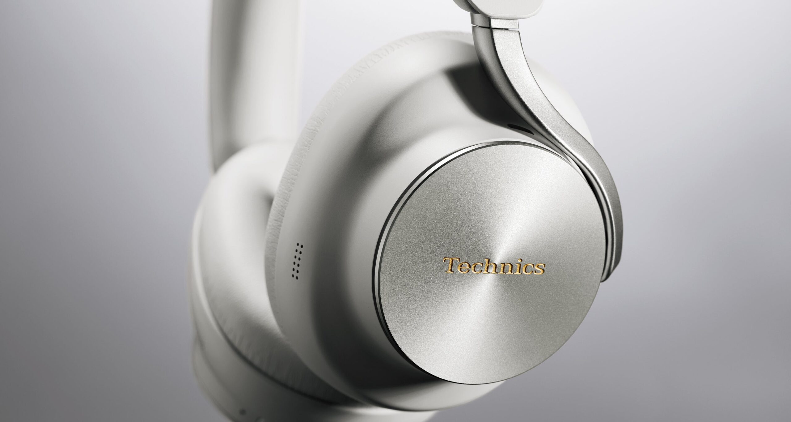 Close-up of the Technics EAH-A1000 Black and Platinum Greige earcups showing the single-sided metal Flow Arm hinge and circular-brushed metal housing plates